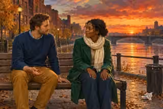 Two friends sit peacefully facing each other on a riverside bench while the sun sets beyond a city bridge.